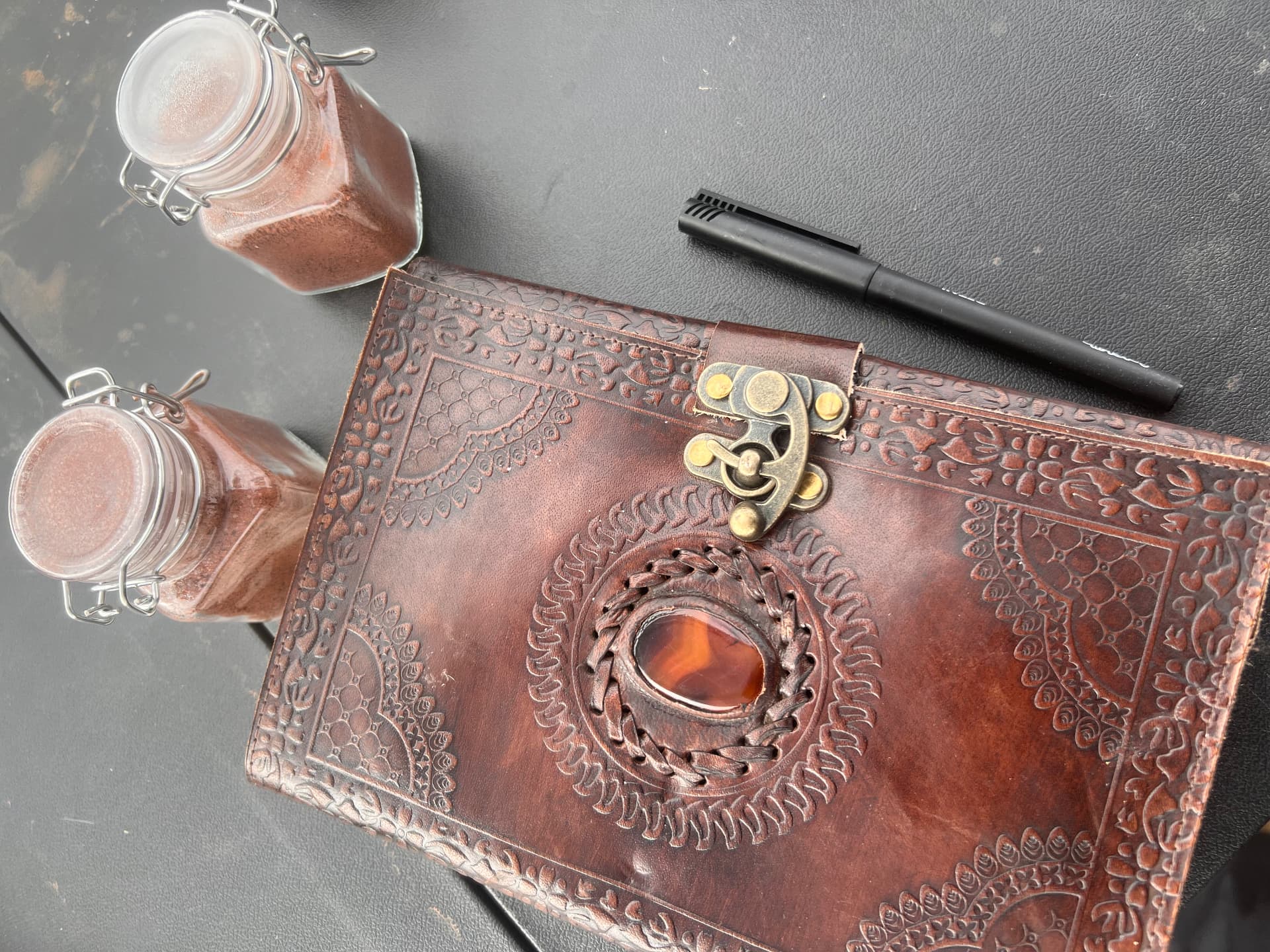Leather-bound prospector journal with a stone inset, beside jars of red claim soil